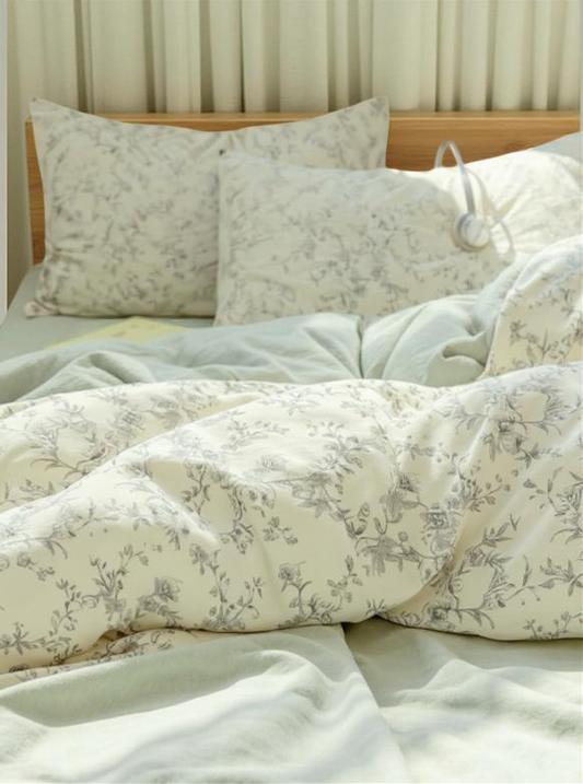 Soft and cozy duvet cover with delicate gray floral pattern on a cream background, being gently held by a hand, showcasing its texture and quality.